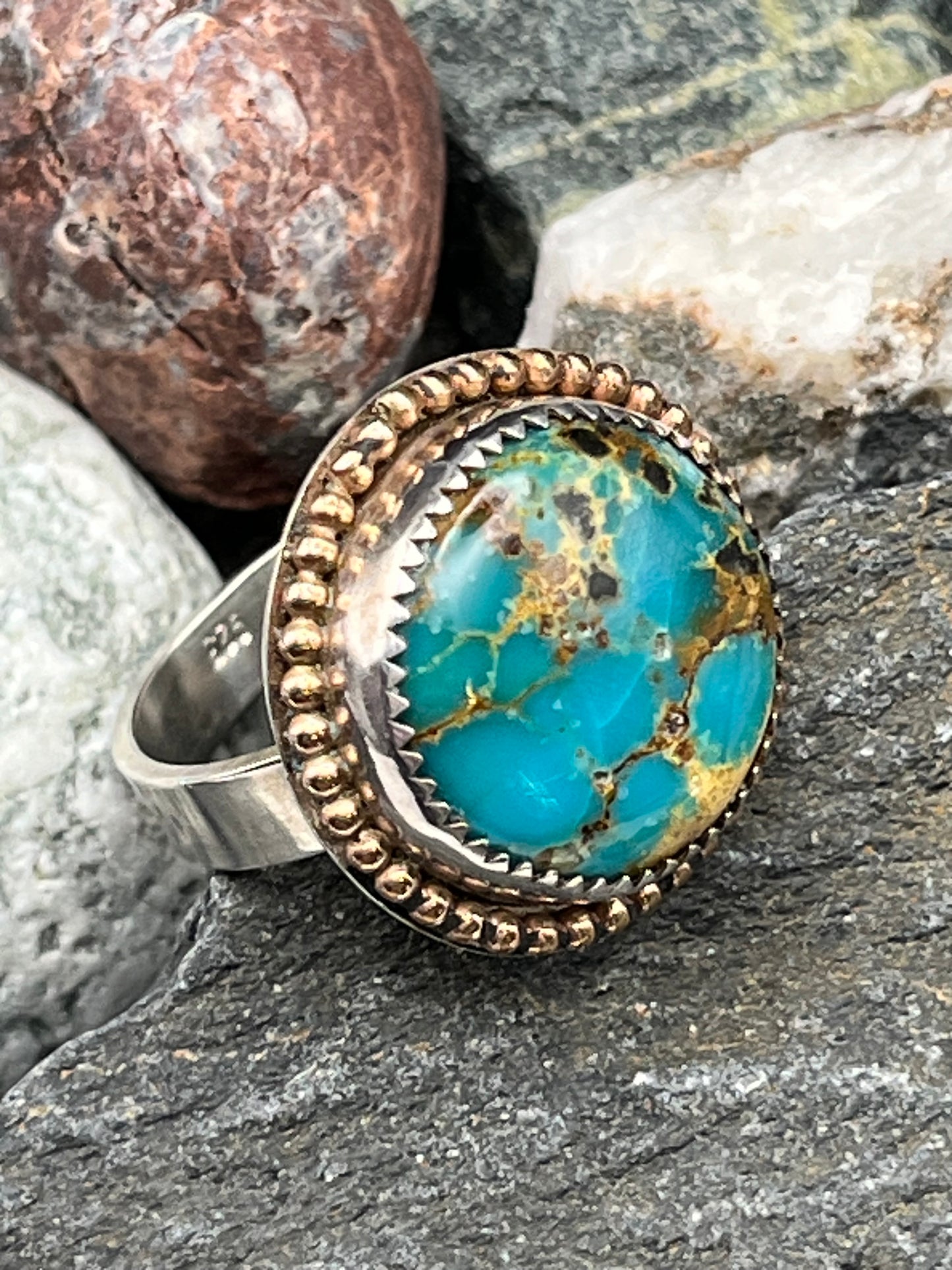 Turquoise stone ring with gold accents on a rock background