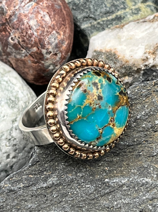 Turquoise stone ring with gold accents on a rock background