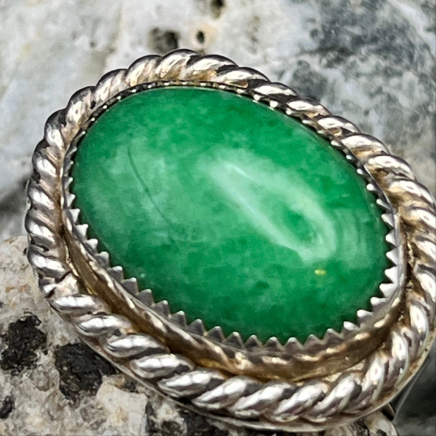 Silver ring with a green stone on a rock background