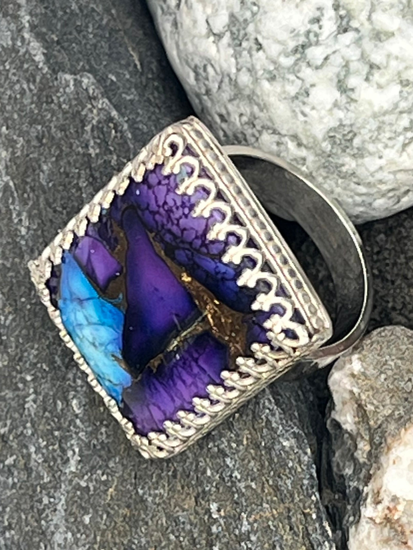 Purple and blue stone in a silver ring on rocks
