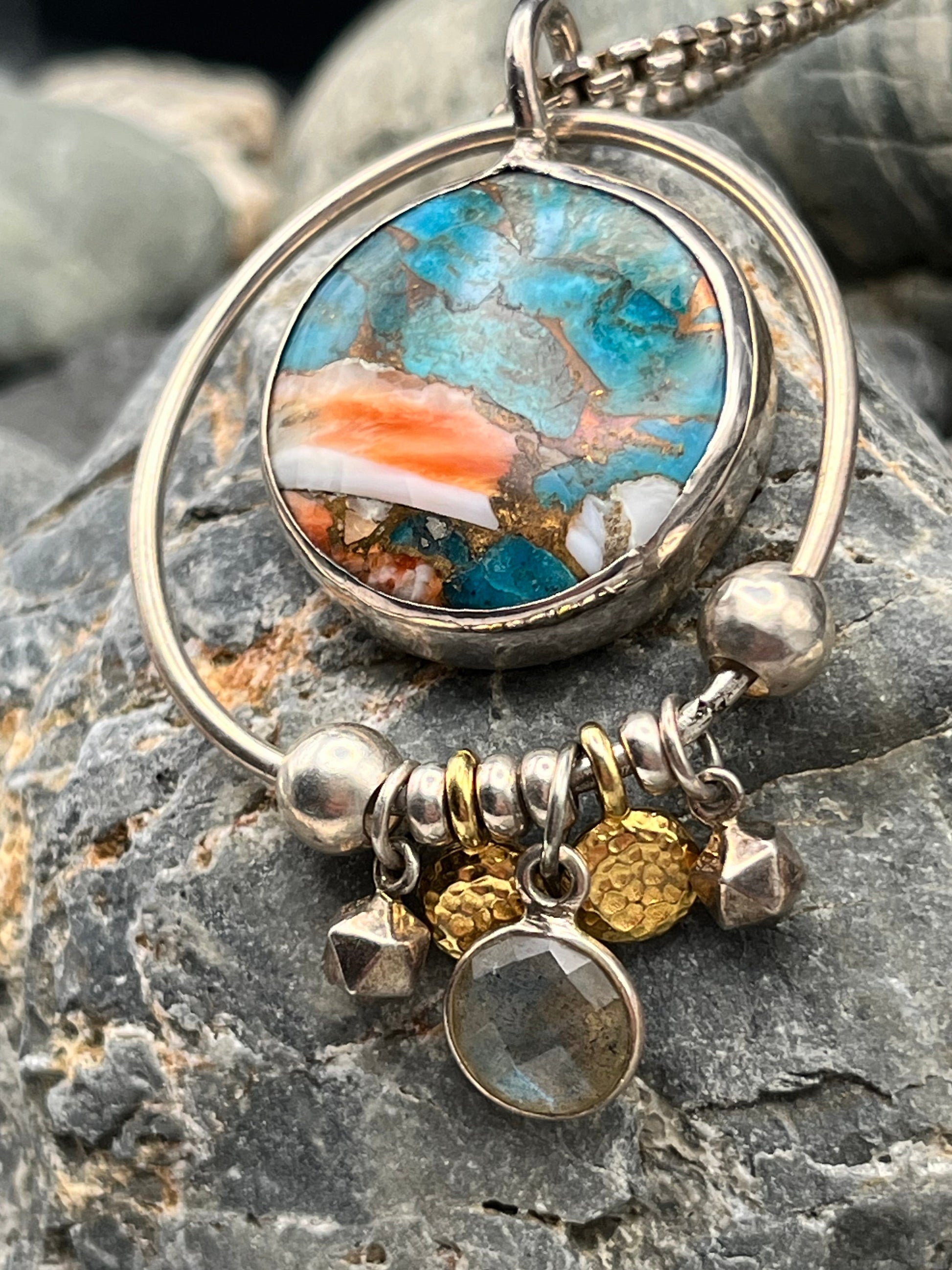 Close-up of a pendant with a colorful stone and gold accents on a rocky surface