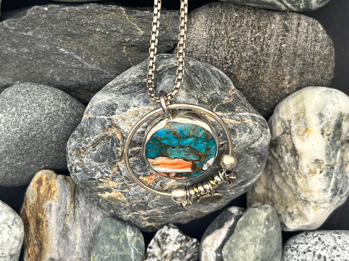 Necklace with a pendant featuring turquoise stone and coral on a bed of rocks